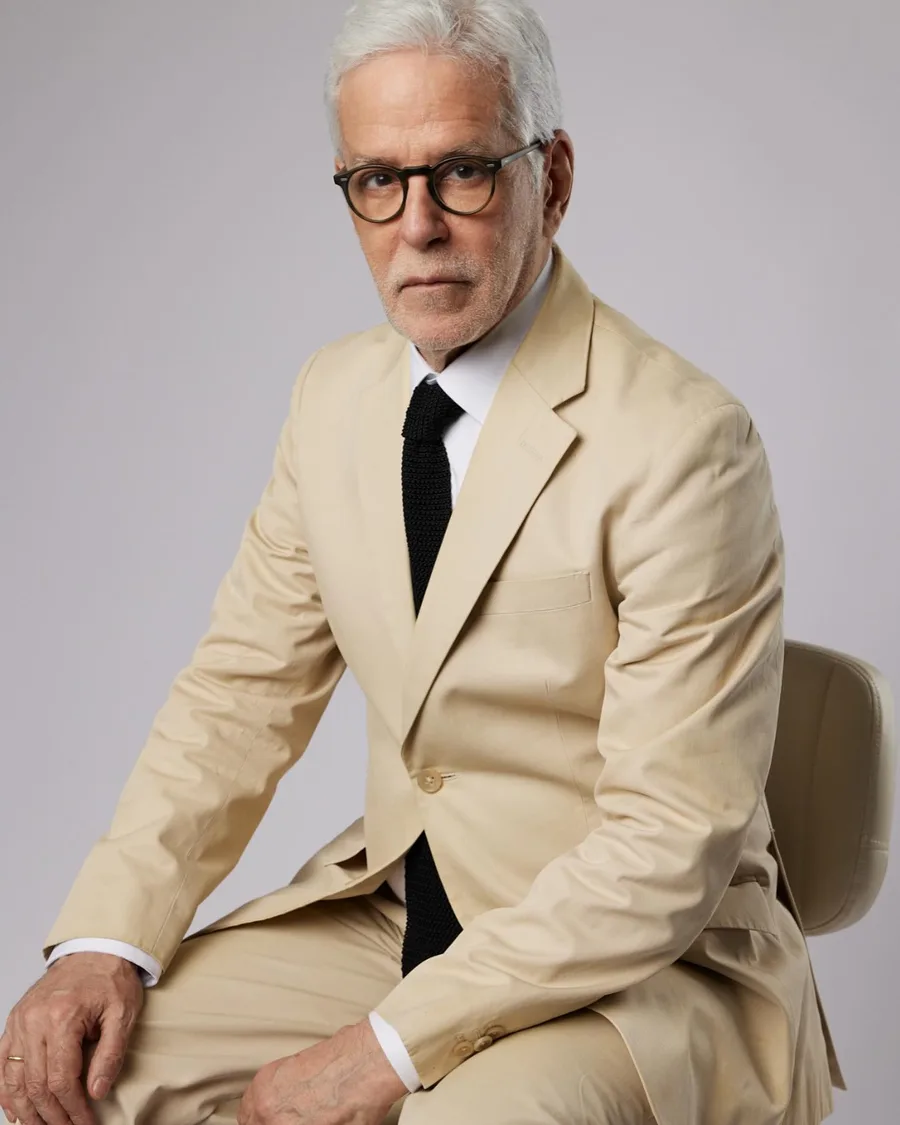 John Amedro seated in a cream suit and knit tie, an editorial portrait
