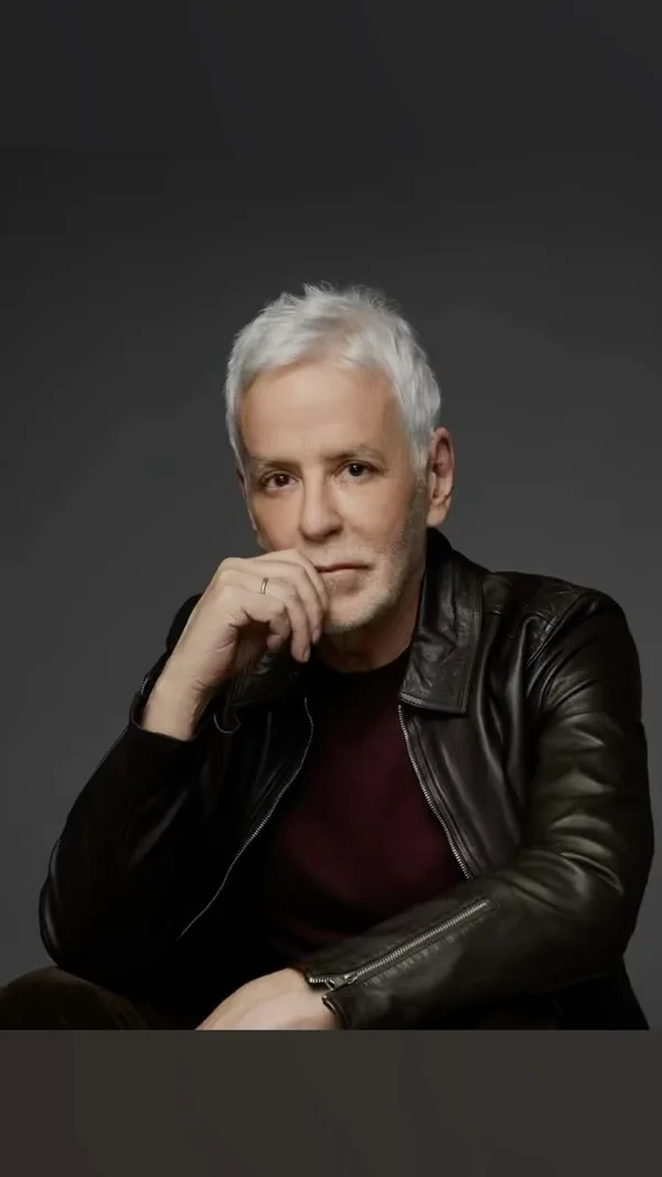 John Amedro in a black leather jacket and oxblood shirt, hand to chin